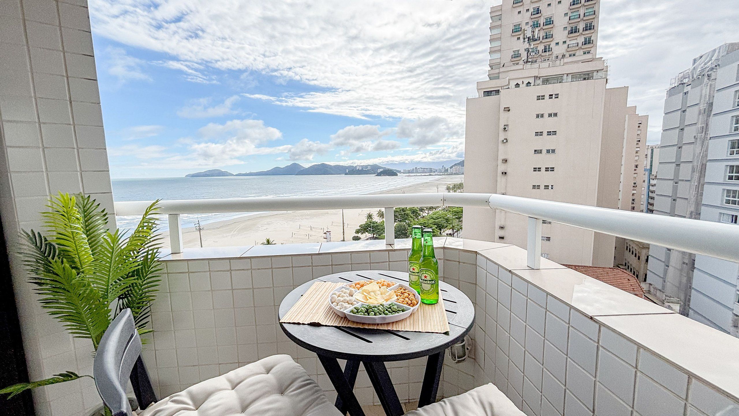 Un balcón con una mesa dispuesta para comer, con vistas a una playa y al horizonte urbano.