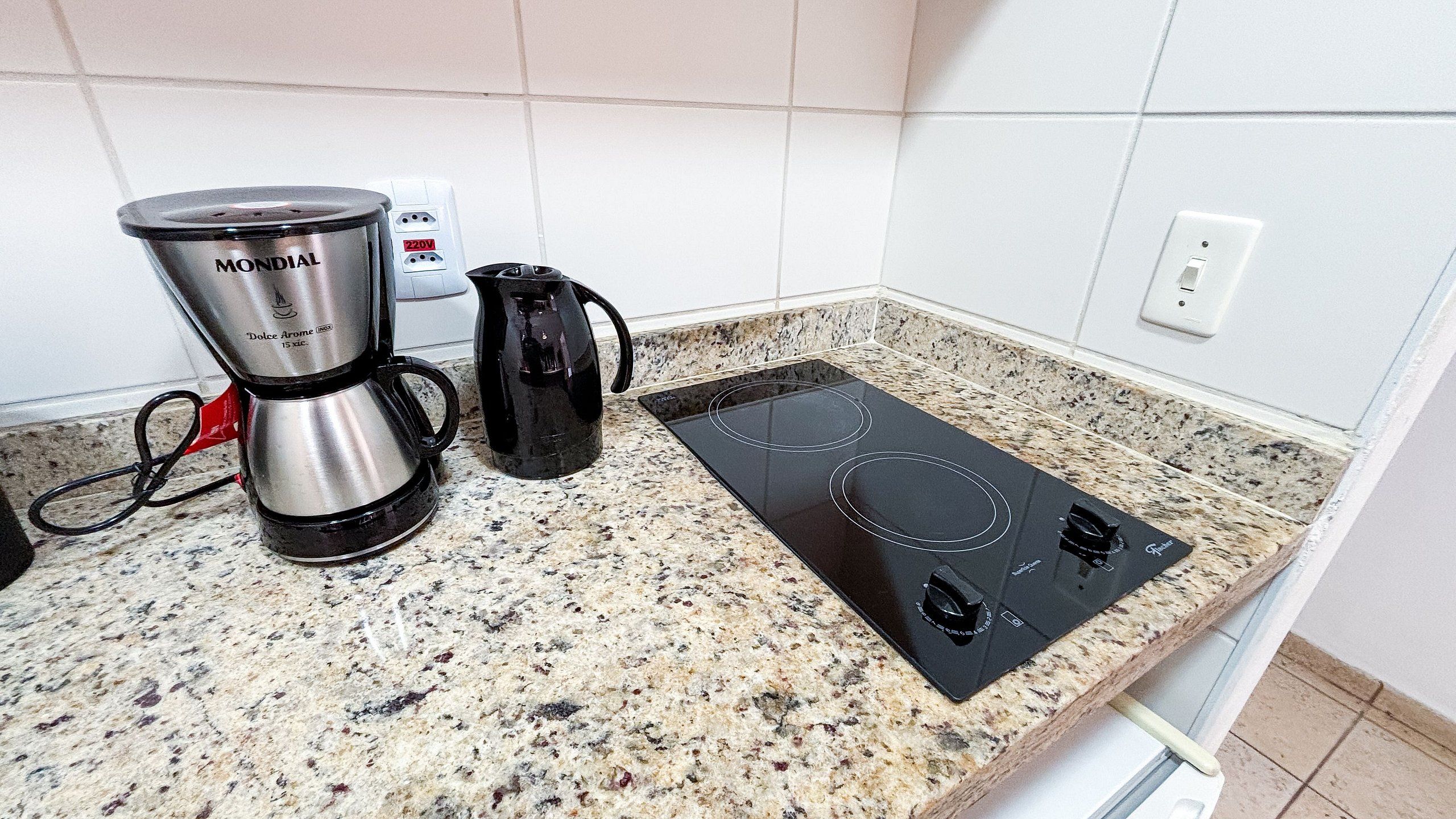 A kitchen with a coffee maker, a kettle, and a stovetop.