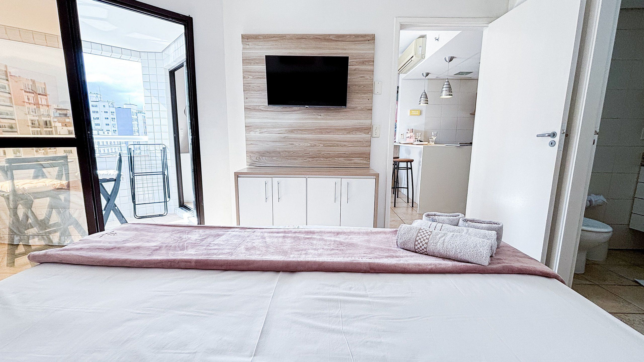 A bedroom with a bed, a television mounted on the wall, and a view of the city through a window.