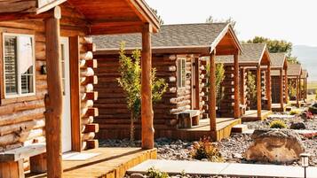 A row of log cabins with wooden decks and small plants in front.