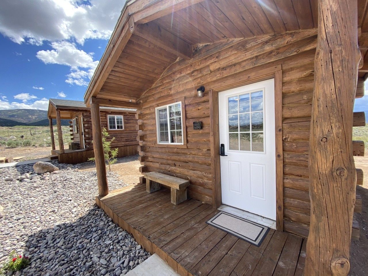 A wooden cabin with a front porch, a bench, and a door.