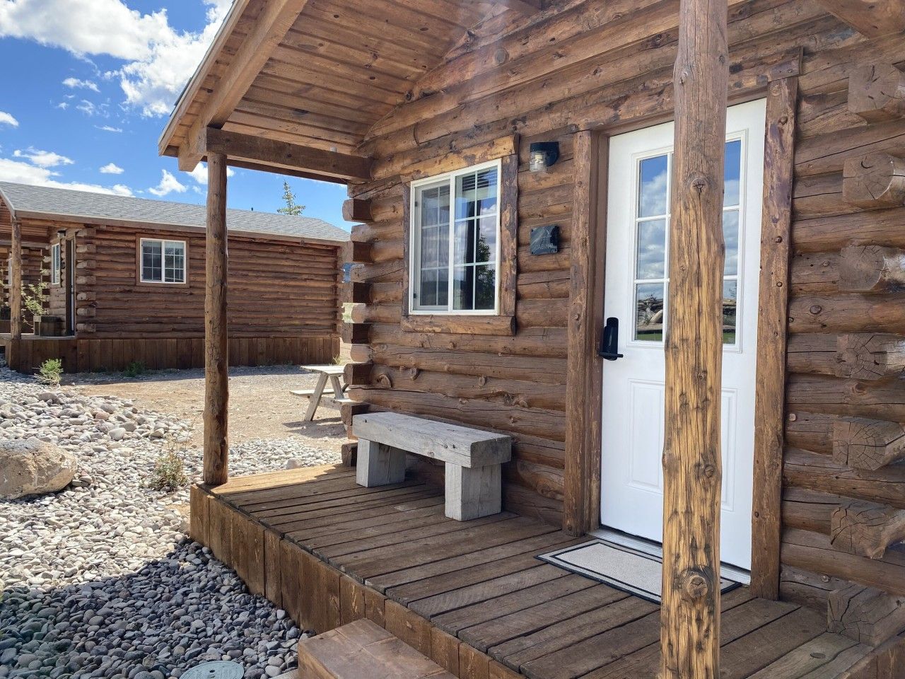 Una cabaña de troncos con un porche de madera, un banco y una puerta.