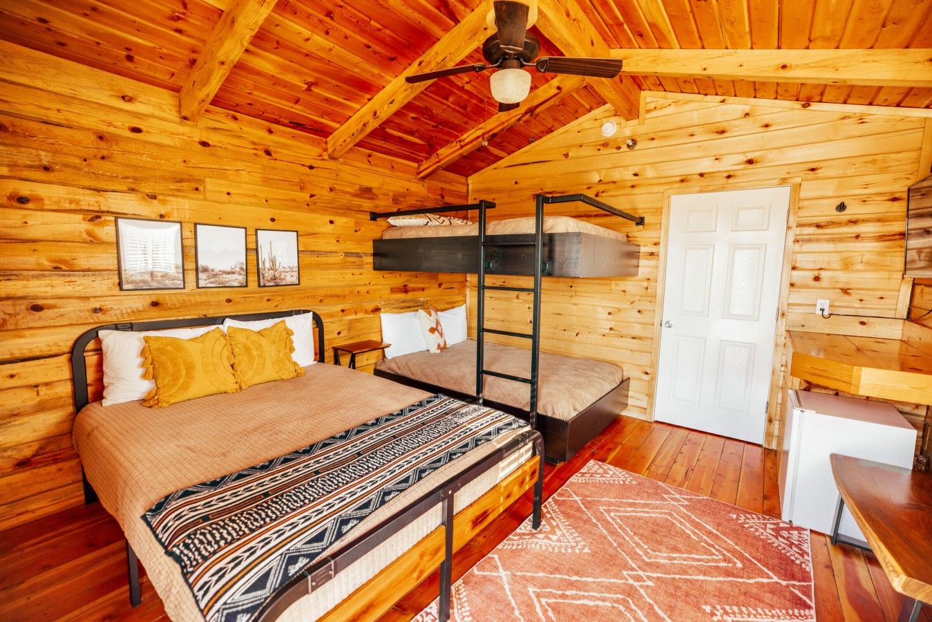 Una habitación tipo cabaña de madera con literas, un escritorio y una puerta.