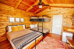 Una habitación tipo cabaña de madera con literas, un escritorio y una puerta.
