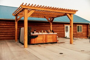 A wooden outdoor hot tub under a pergola with a log cabin in the background. - Lyman cowboy cabin with hot tub access (Lyman)