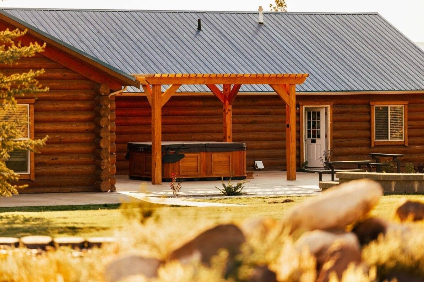 A log cabin with a covered patio, outdoor seating, and a hot tub.