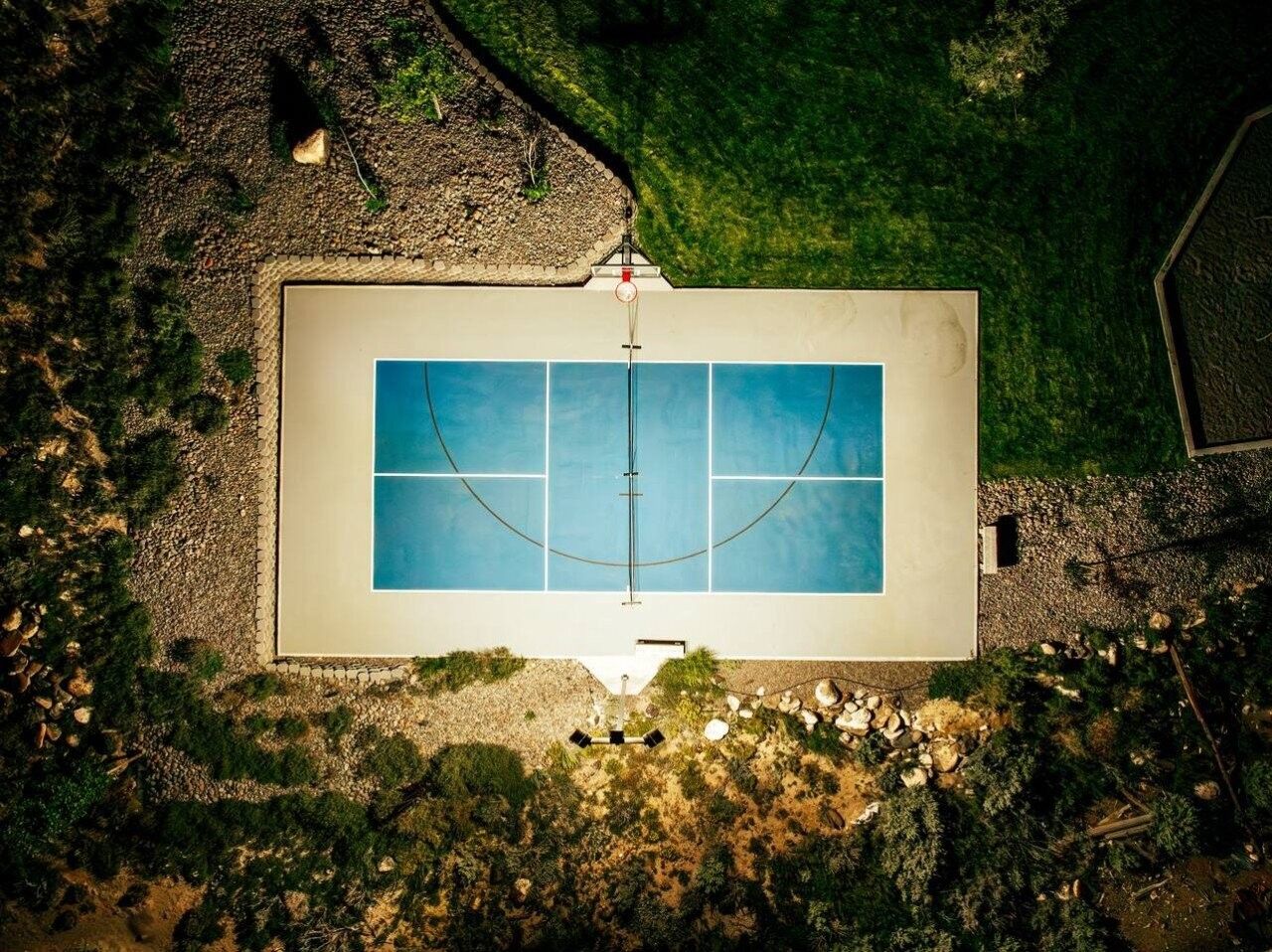 An aerial view of a rectangular swimming pool with a surrounding deck, surrounded by a landscaped garden with various plants and a pebble path.
