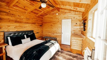 A wooden cabin bedroom with a bed, a ceiling fan, a door, and a window.