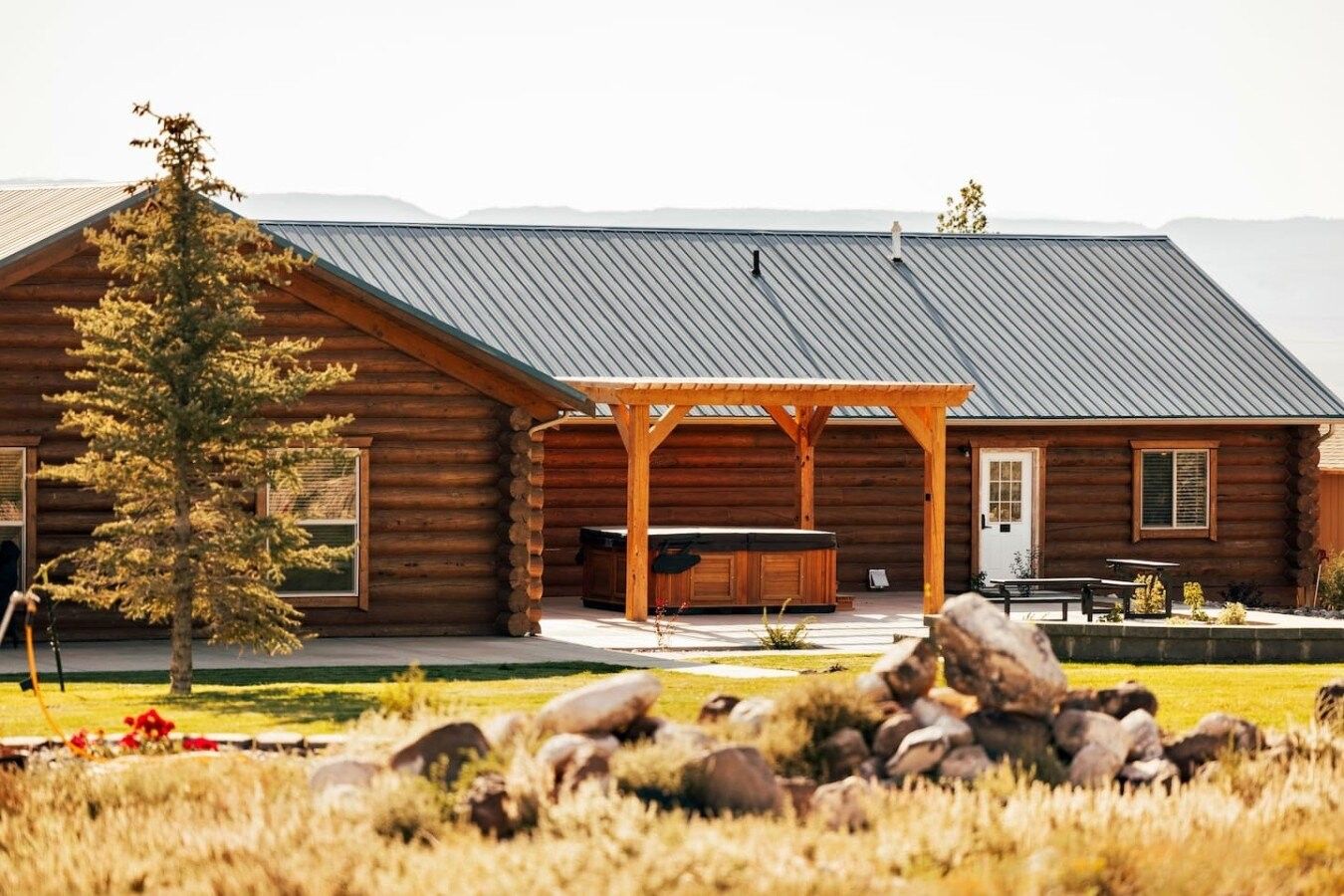 A log cabin with a covered patio, a hot tub, and a stone fireplace.