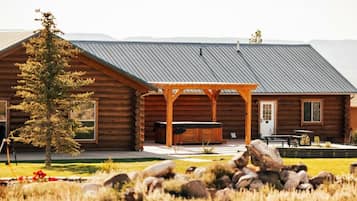 A log cabin with a covered patio, a hot tub, and a stone fireplace.
