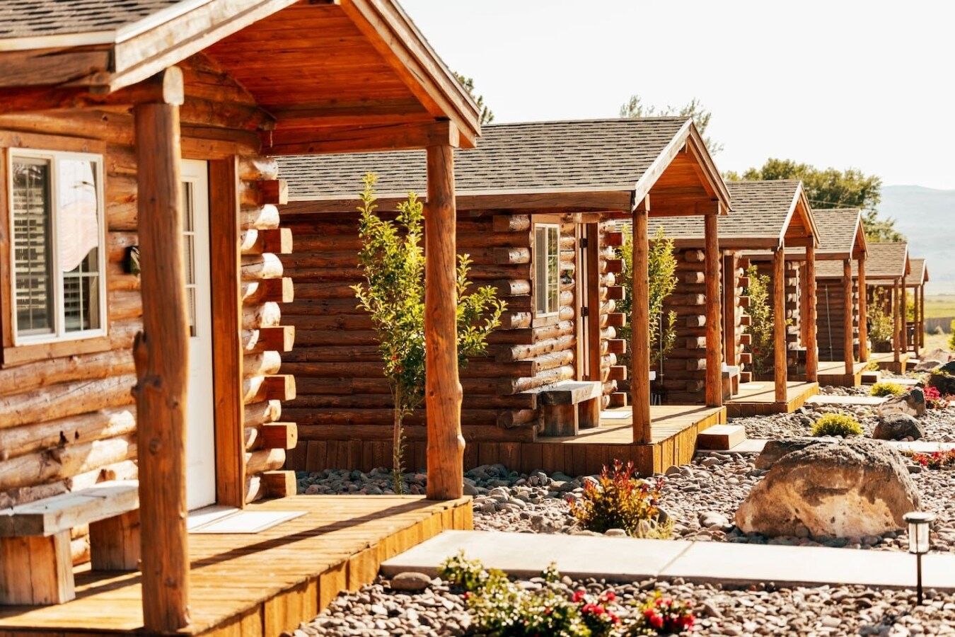 A row of log cabins with wooden decks and small plants in front.