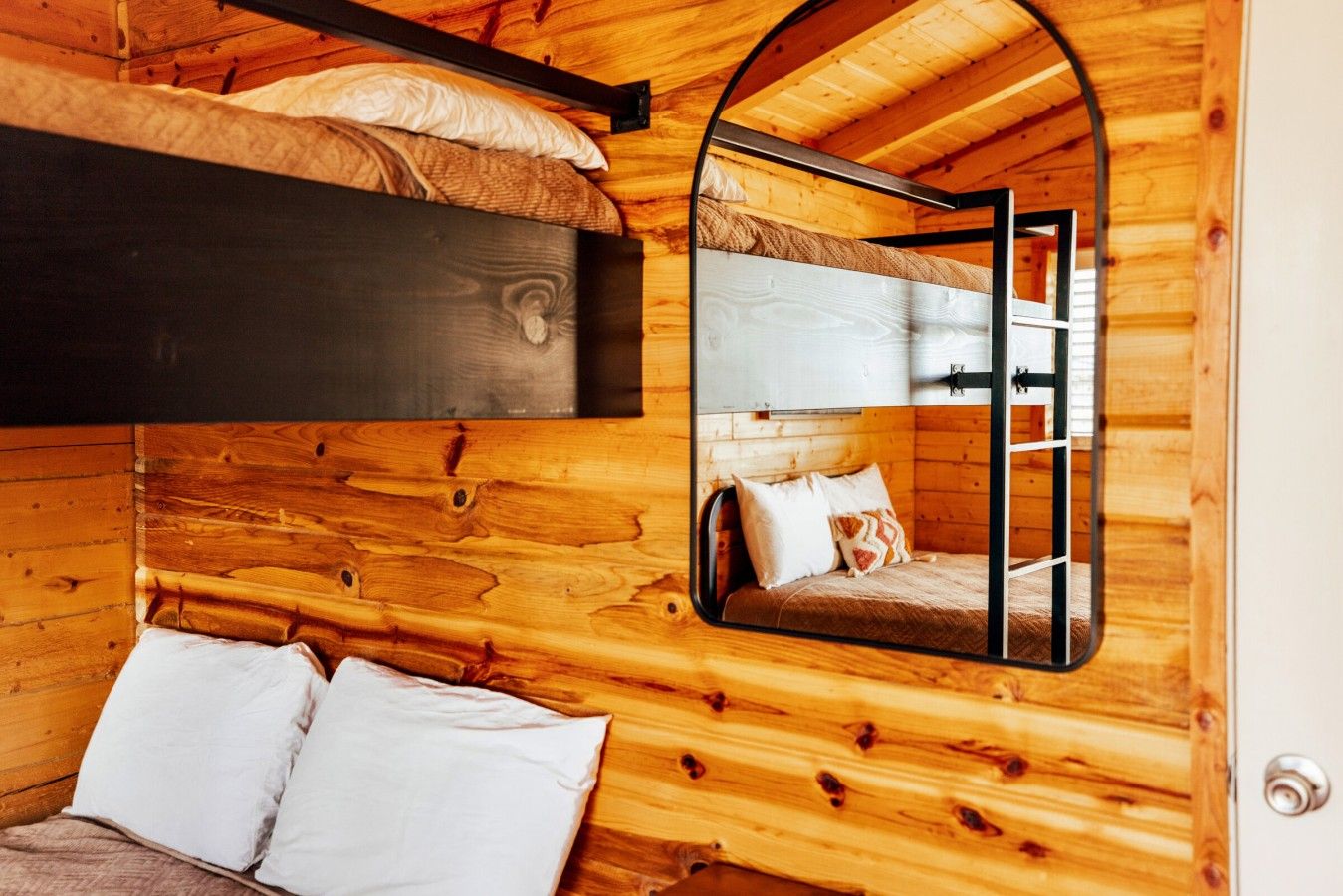 Un intérieur en bois avec un lit superposé, un miroir qui reflète la pièce et une porte.