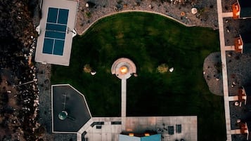 An aerial view of a property with a tennis court, a circular fountain, and outdoor seating areas.