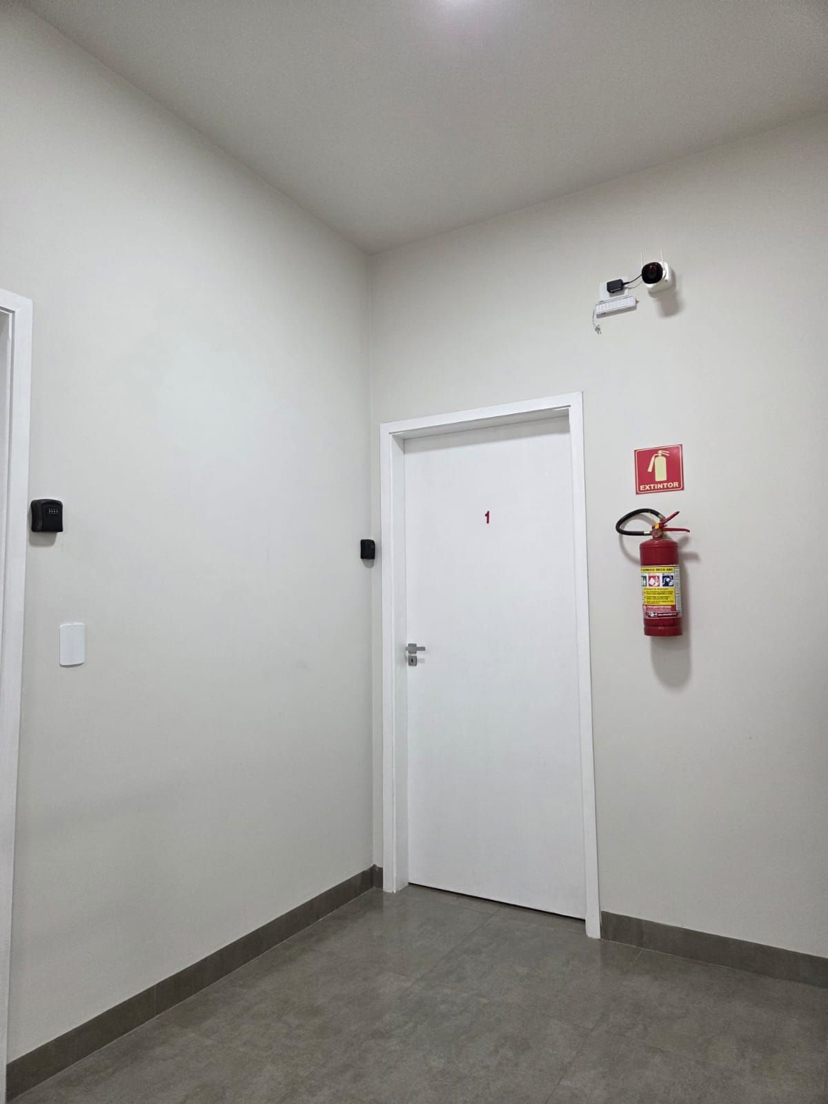 A hallway with a white door, a fire extinguisher mounted on the wall, and a smoke detector.