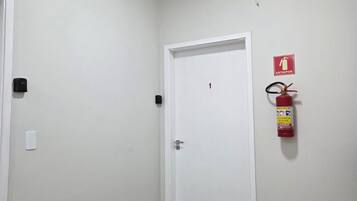 A hallway with a white door, a fire extinguisher mounted on the wall, and a smoke detector.