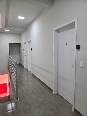 A corridor with white doors, a metal railing, and a red-lit area at the end.
