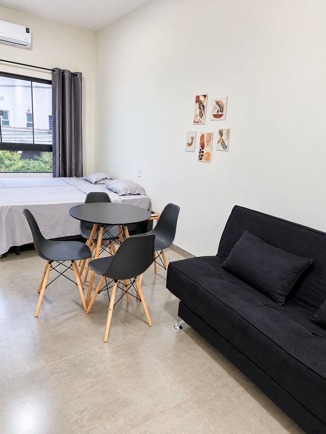 A modern hotel room with a bed, a round dining table with chairs, a black sofa, and artwork on the wall.