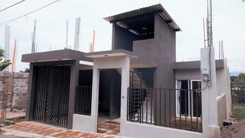 A modern two-story house with a flat roof, a gated entrance, and a visible staircase leading to the upper floor.