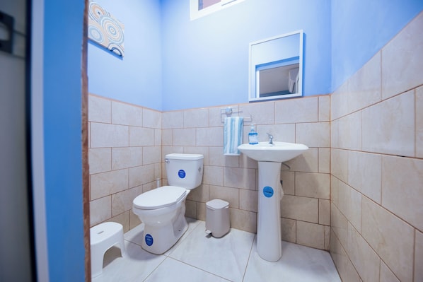 A bathroom with two toilets, a sink, and a small trash bin.