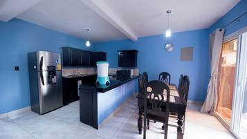 A modern kitchen with a dining area, featuring a refrigerator, stove, and a coffee machine.