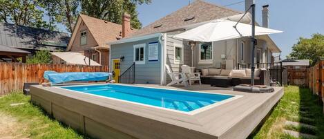 A backyard with a swimming pool, a covered patio, and a wooden deck.
