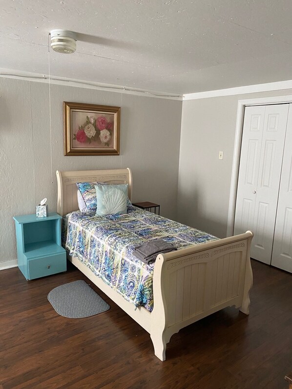 Un dormitorio con una cama, una mesita de noche, un tapete, una puerta y una lámpara de pared.
