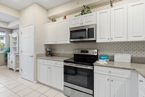 A modern kitchen with white cabinetry, a built-in microwave, a stove, and a coffee maker. - #1013 - First Floor - Lake View - Walk to Golf (Naples)