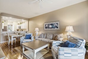 A living room with a dining area, a kitchen in the background, and a ceiling fan. - #1013 - First Floor - Lake View - Walk to Golf (Naples)