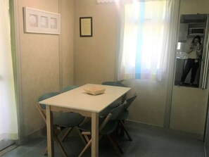 Un petit espace de restauration privatif, avec une table et quatre chaises. Un certificat encadré est accroché au mur, et il y a une fenêtre avec des rideaux.