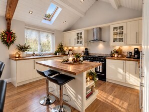 A modern kitchen with a central island, bar stools, a stove, and a skylight. - The Granary | Luxury Countryside Retreat (Maidstone)