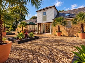 A two-story house with a patio area, surrounded by potted plants and a gravel driveway. - The Granary | Luxury Countryside Retreat (Maidstone)
