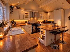 Une cuisine moderne avec des plans de travail en bois, un îlot central doté de tabourets, des meubles blancs et un éclairage sous les meubles.