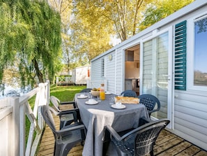 A deck with a table set for two, chairs, and a view of a mobile home. - Mobile home with AC - 6 guests (Badefols-sur-Dordogne)