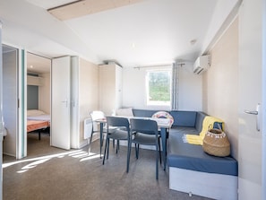 A compact room with a bed, a table with chairs, a sofa, and a window. - Mobile home with AC, pets welcome - 6 guests (Badefols-sur-Dordogne)
