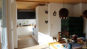 Cozinha moderna com armários brancos, teto de madeira e área de jantar com mesa posta para dois.