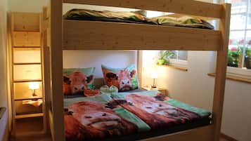 Una cama litera con colcha temática de vaca, una lámpara de noche y una ventana con flores.