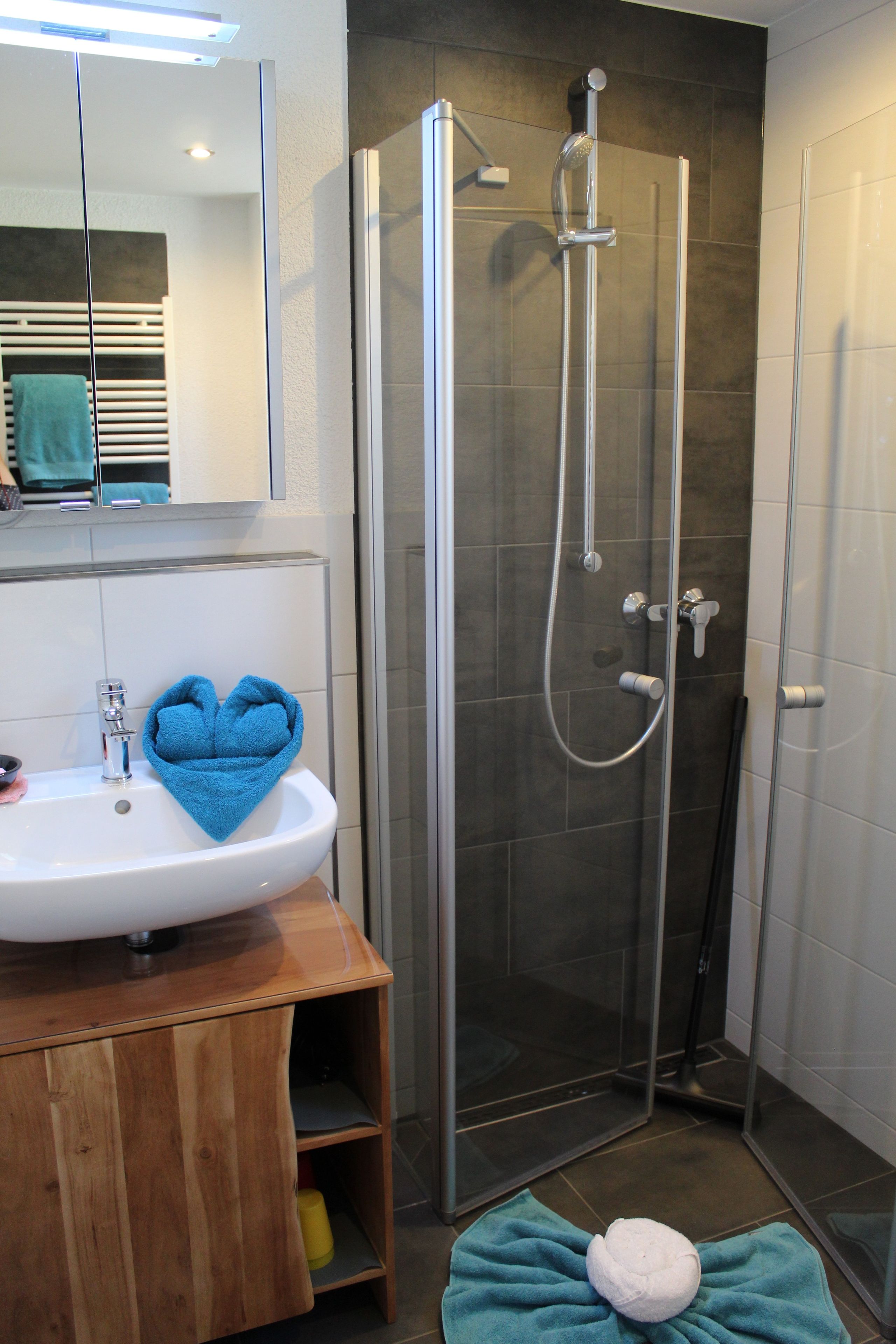 Un baño con ducha de vidrio, un lavamanos con una toalla azul y un tocador de madera.