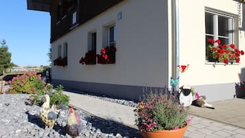 Un edificio con fachada blanca, varias ventanas y jardineras con flores rojas.