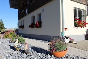 Un edifici amb façana blanca, diverses finestres i balcons amb flors vermelles.