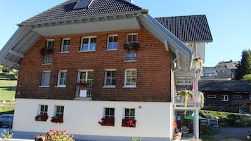 A multi-story building with a sloped roof, multiple windows, and flower boxes.