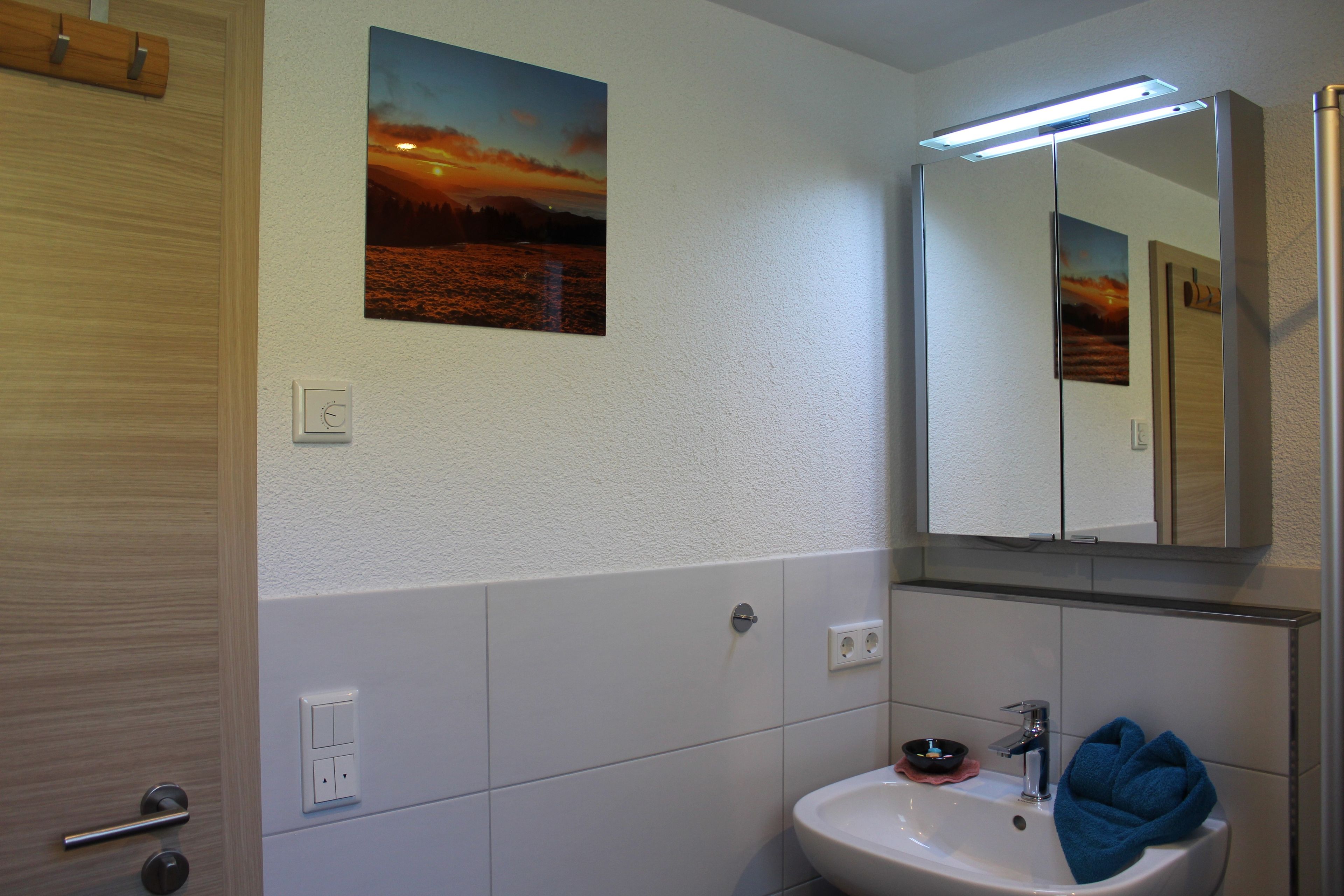 Ein Badezimmer mit Waschbecken, Spiegel und einem Sonnenuntergangsbild.