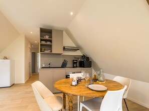 A modern kitchen with a dining area, featuring a round wooden table, white chairs, and a built-in oven. - Renovated apartment in town center (La Chapelle-Launay)