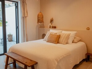 A bedroom with a bed, a bench, a potted plant, and a door leading to an outdoor area. - Lodge with private pool, nature - 4 guests (Salazie)