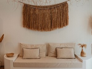 A neutral-toned sofa with two pillows, a woven wall hanging, and a small vase with dried plants. - Lodge with private pool, nature - 4 guests (Salazie)