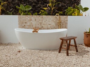A freestanding bathtub with a tiled wall behind it, a small wooden stool, and a potted plant to the right. - Lodge with private pool, nature - 4 guests (Salazie)