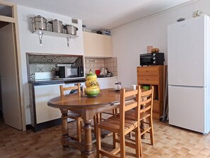 A compact kitchen with a wooden dining table, chairs, a microwave, a refrigerator, and a shelf with pots and pans. - F1 cabin with AC and parking - 5 guests (Canet-en-Roussillon)