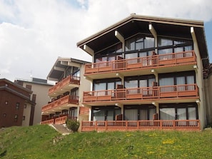 A multi-story hotel with balconies, a staircase leading to the entrance, and a grassy area in front. - Sunny studio with balcony - 4/5 guests (Montvalezan-La Rosière)