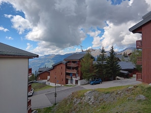 A residential area with wooden houses, a blue car parked in front, and mountains in the background. - Sunny studio with balcony - 4/5 guests (Montvalezan-La Rosière)