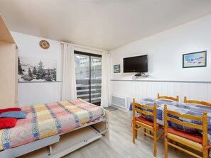 Un dormitori amb un llit, una taula, un televisor i una finestra que mostra un paisatge nevós.