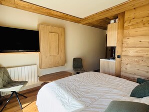 A bedroom with a bed, a chair, a TV, and wooden paneling. - Cozy apartment mountain view - 2 guests (Notre-Dame-de-Bellecombe)